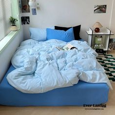 an unmade bed with blue sheets and pillows in a white room next to a window