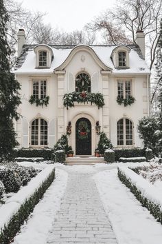 a white house covered in snow with wreaths on the front door and walkway leading up to it