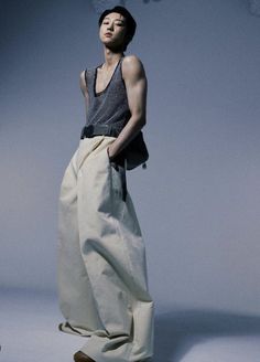 a man standing in front of a gray background wearing white pants and a tank top