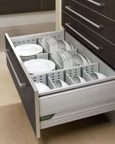 an open drawer with plates and cups in it on the floor next to a dresser