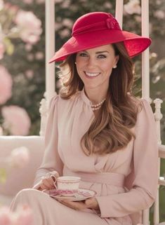 a woman in a pink dress and red hat sitting on a porch swing holding a cup