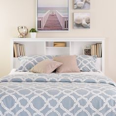 a bed with a blue and white comforter on it next to a book shelf