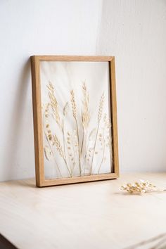 a wooden frame sitting on top of a white table next to a flower vase and dried plant