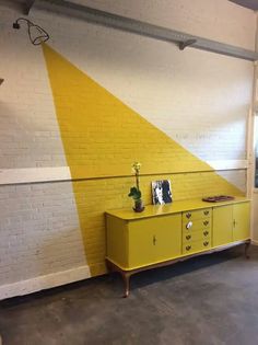 a yellow cabinet in front of a white brick wall with an arrow painted on it