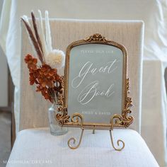 there is a sign that says guest book and flowers in a vase on the back of a chair