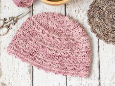 a crocheted pink hat sits next to a pair of scissors and some yarn