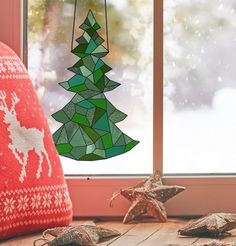 a christmas tree made out of stained glass hanging from a window sill next to ornaments