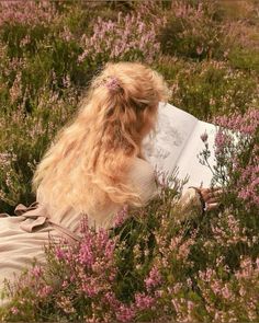 a woman sitting in the grass reading a book with her hair blowing back and eyes closed