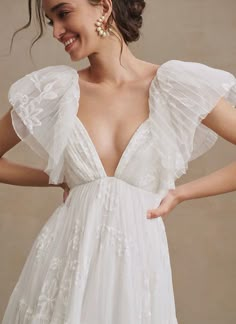 a woman wearing a white dress with ruffles on the shoulders and an open back