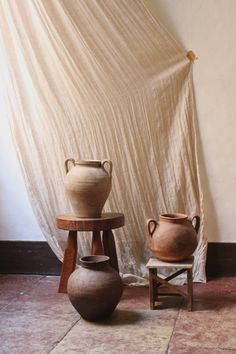 two vases sitting next to each other in front of a white drapeed wall