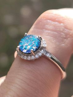 a close up of a person's hand holding a ring with a blue stone