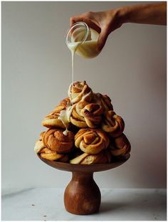 a person pouring cream on top of cinnamon buns in a wooden bowl with other pastries