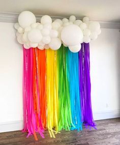 balloons and streamers are hanging from the ceiling in front of a rainbow colored wall