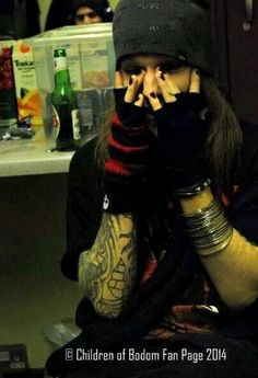 a man with long hair wearing a beanie and holding his hands to his face