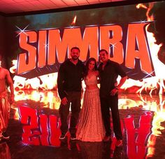 three people posing for a photo in front of a sign that says simba on fire