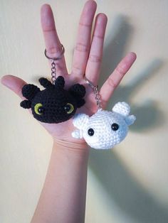 a hand holding two small crocheted items in the shape of animals, one black and one white