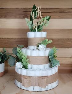 a three tiered diaper cake is decorated with greenery and burlocks