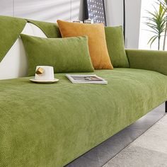 a green couch with two pillows and a magazine on the arm rest in front of it