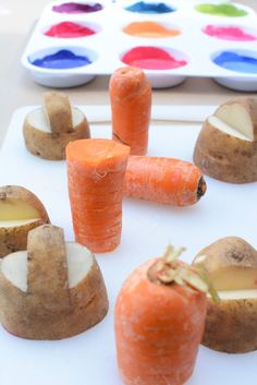 carrots, potatoes and other food items on a white surface with paint palettes in the background