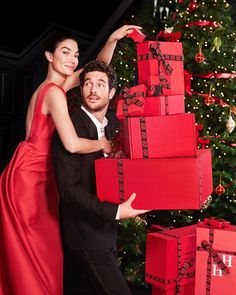 a man and woman are posing with presents in front of a christmas tree