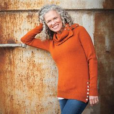 a woman in an orange sweater leaning against a rusty wall