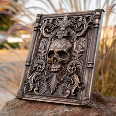 an intricately carved book with a skull on it's cover sitting on top of a rock