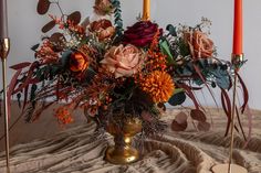 a vase filled with lots of flowers on top of a table next to two candles