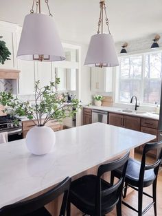 a kitchen with two lamps hanging over the island and three chairs around the table in front of it