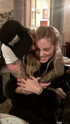 a man and woman hug each other while sitting in a room with food on the table