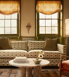 a living room filled with furniture and two windows covered in shades of brown, white and tan