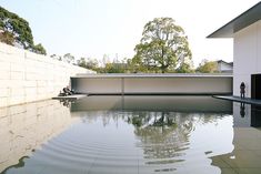 an empty swimming pool in front of a white building with trees on the other side