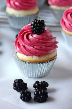 some cupcakes with pink frosting and blackberries on the top are ready to be eaten