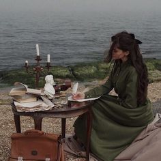 a woman sitting at a table in front of the ocean with an open book on it