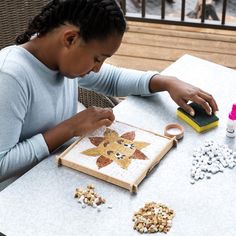 a woman sitting at a table working on a craft project with beads and glues