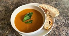 a white bowl filled with soup next to a piece of bread on top of a table