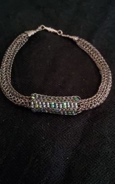 a silver chain bracelet with green and white beads on it's end, sitting on a black surface