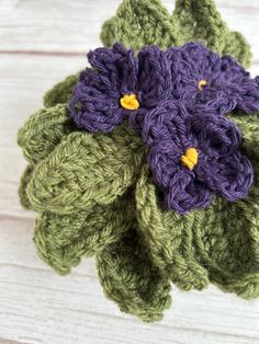 a crocheted flower with purple and green flowers on it's center sits on a white wooden surface