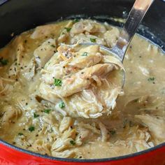 a red pot filled with chicken and dumpling in gravy on top of a wooden table