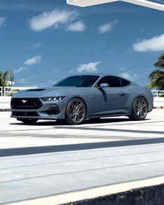 a gray mustang parked in front of a gas station with blue sky and clouds behind it