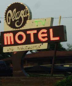 a neon sign for a motel with cars in the background