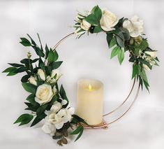 a candle and some white flowers on a table next to a wreath with greenery