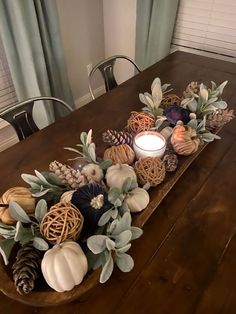 a wooden table topped with a centerpiece filled with pine cones, pumpkins and greenery