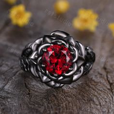 a red stone ring sitting on top of a piece of wood with yellow flowers in the background