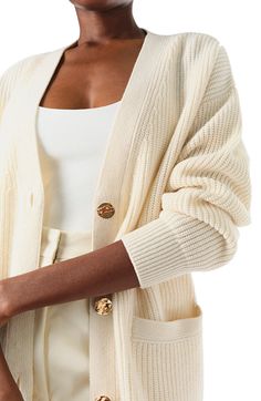 Monique Lhuillier Spring 2024 white cashmere long chunky cardigan with gold buttons - front crop. White Cashmere Cardigan With Button Closure, Luxury Beige Cardigan, Cream Cashmere Outerwear With Button Closure, Cream Cashmere Cardigan For Daywear, Chic Cream Cashmere Cardigan, Elegant Cream Sweater With Button Closure, Luxury Fall Cardigan With Buttons, Luxury Buttoned Cardigan For Fall, Luxury Cashmere Cardigan With Button Closure