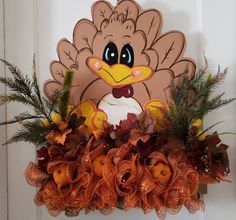 a decorated turkey head hanging on a door with fall leaves and flowers in the foreground