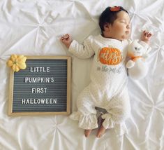 a baby is laying next to a sign that says little pumpkin's first halloween