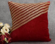 a red and gold pillow sitting on top of a gray couch next to white flowers