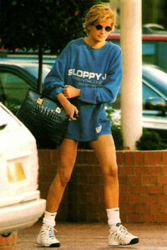 a woman in blue shirt and shorts walking down the street with her hand on her hip