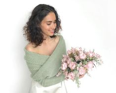 a woman holding a bouquet of pink roses in her right hand and wearing a green off the shoulder sweater