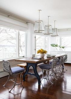 a dining room table with chairs and a vase on top of it in front of large windows